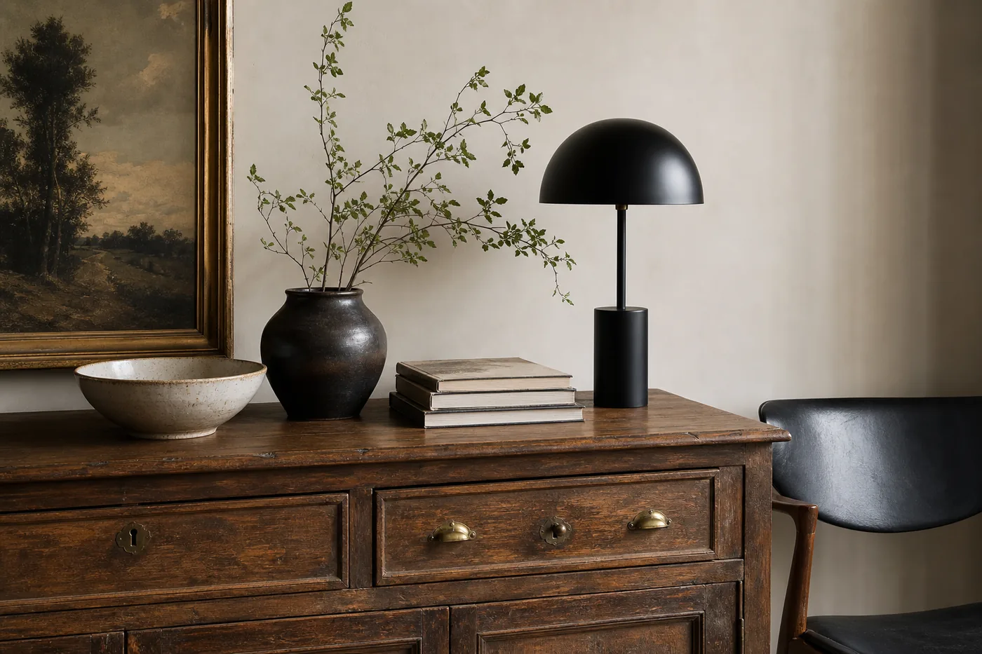A vintage wood sideboard styled with a modern black lamp, old framed art, ceramics, and warm materials